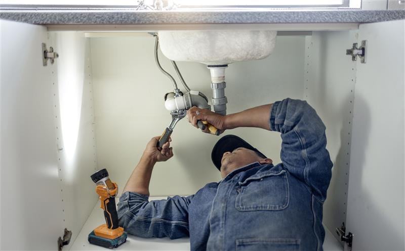 Plumber repairing pipes beneath a bathroom sink in Palm Springs