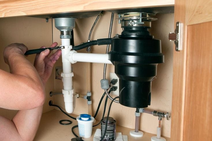 Plumber installing a garbage disposal beneath a kitchen sink in Palm Springs