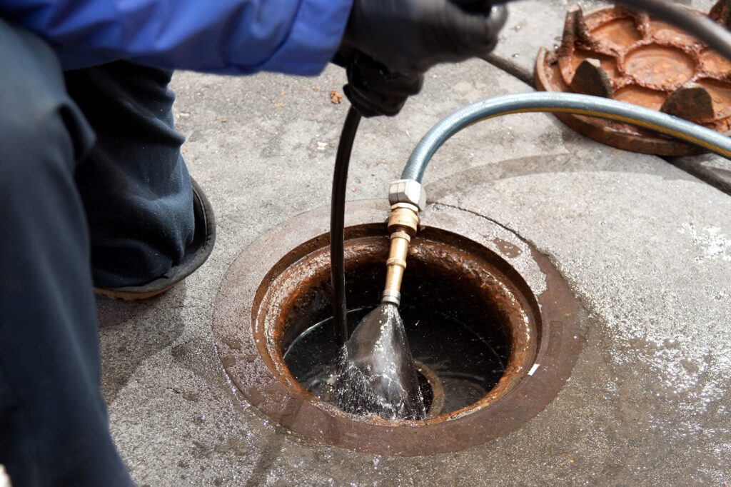 Plumber hydro jetting a sewer line through a manhole in Palm Springs
