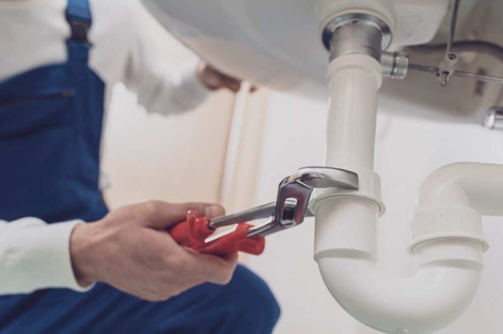 Plumber repairing a white drain pipe beneath a sink in Palm Springs