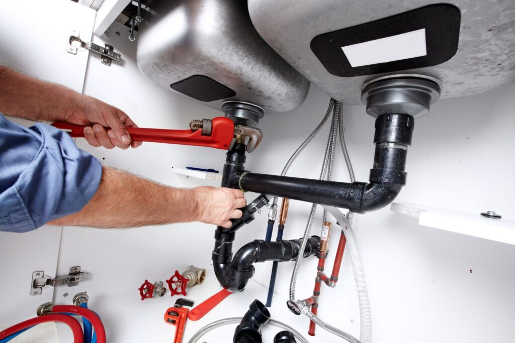 Plumber repairing drain pipes beneath a kitchen sink in Palm Springs